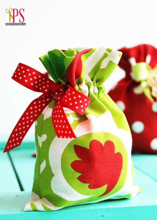 Drawstring gift bag, green white and red pattern with red ribbon with white dots on blue table.